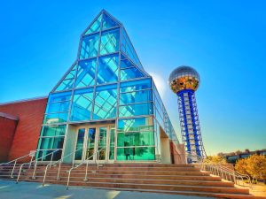 Exterior of the Knoxville Convention Center with its glass entrance and the Sunsphere tower behind it. Link to the convention center website, opens in a new tab.